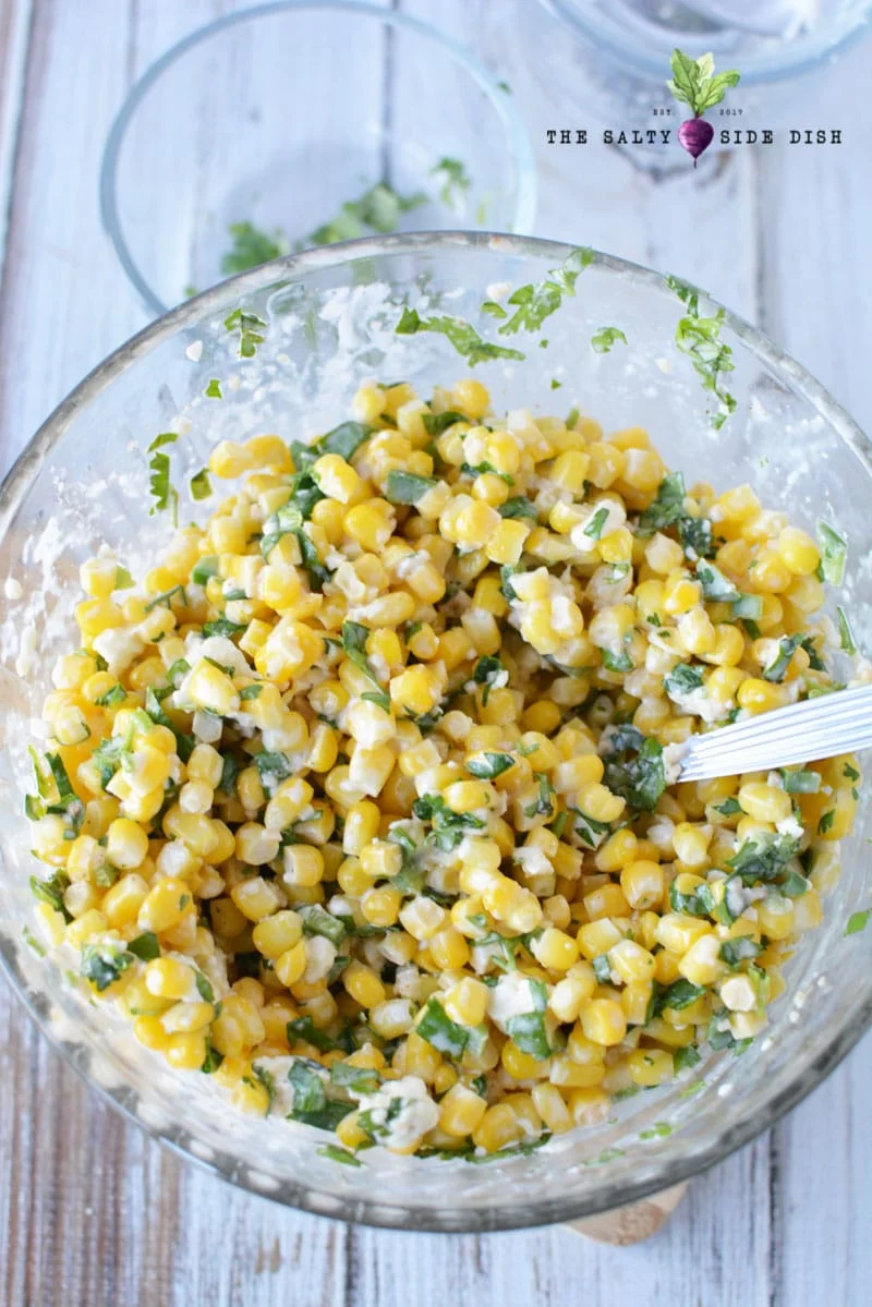 mexican corn salad all mixed in a bowl with a spoon ready to serve as a side dish