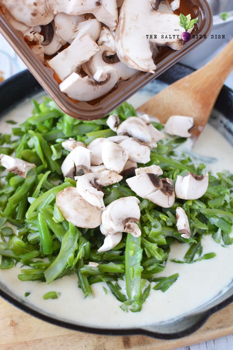 homemade green bean casserole with fresh mushrooms being poured into cast iron pan