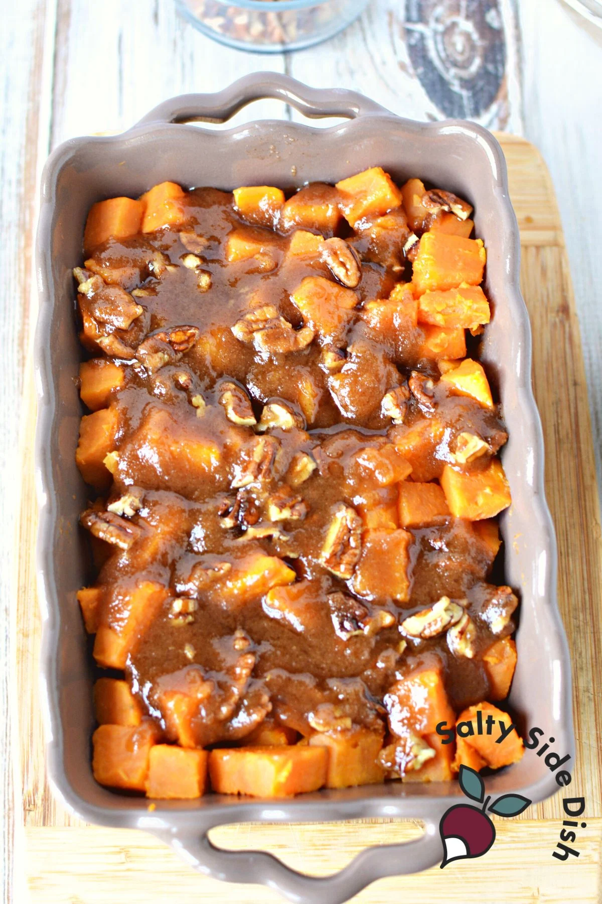 layer brown sugar on cut and boiled sweet potatoes in a gray baking dish.