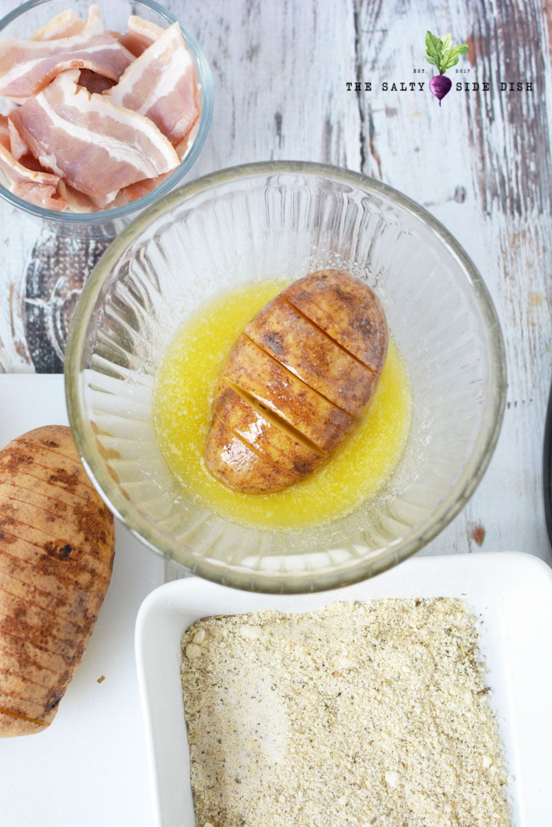 hasselback stuffed potatoes laying in a bowl of butter