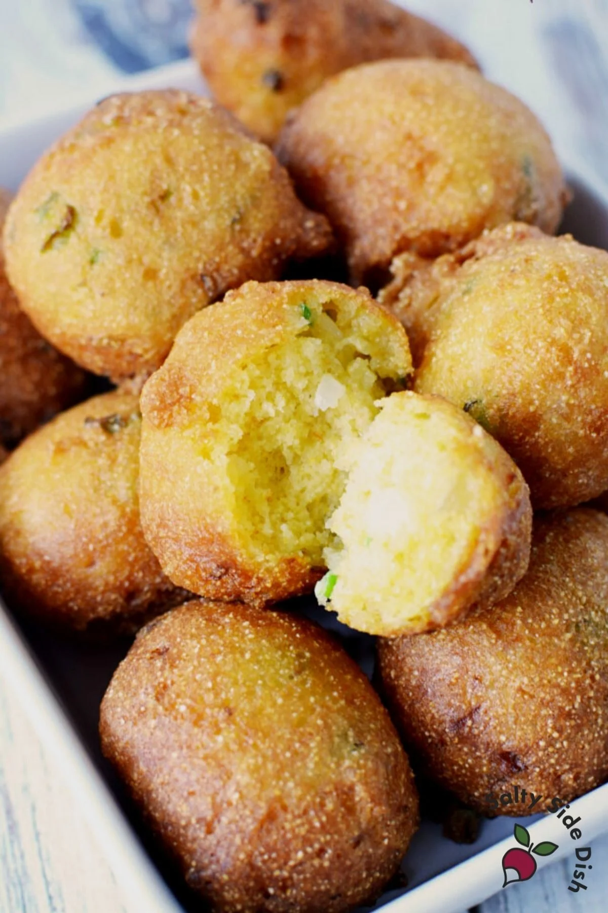 pile of hush puppies on a white plate with one split open showing a center.