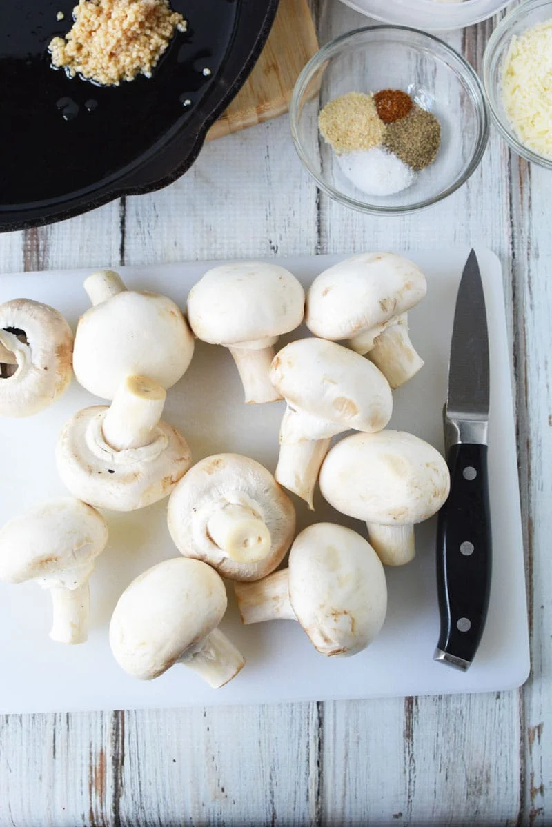 stuffed mushroom recipe with freshly uncut mushrooms laying on a cutting board