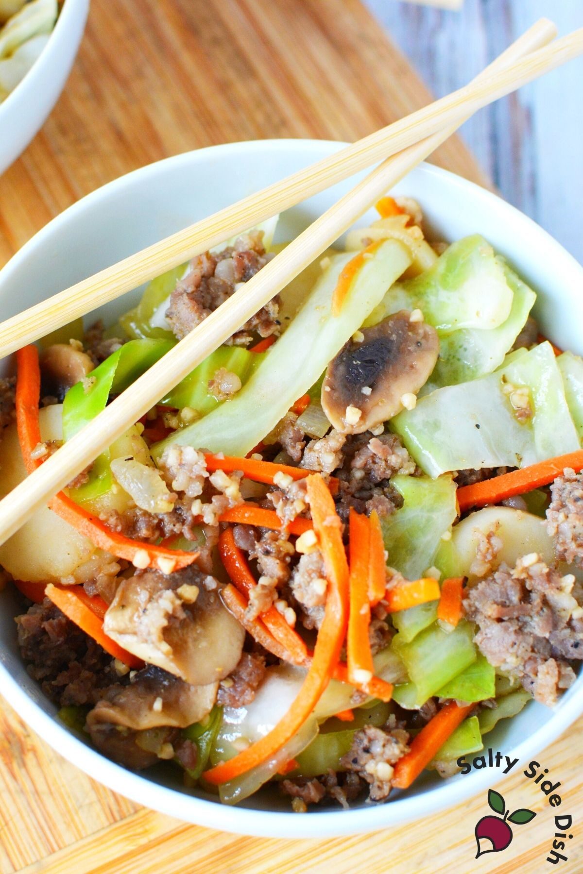 sausage egg roll with shredded cabbage in a white bowl with chopsticks on top.