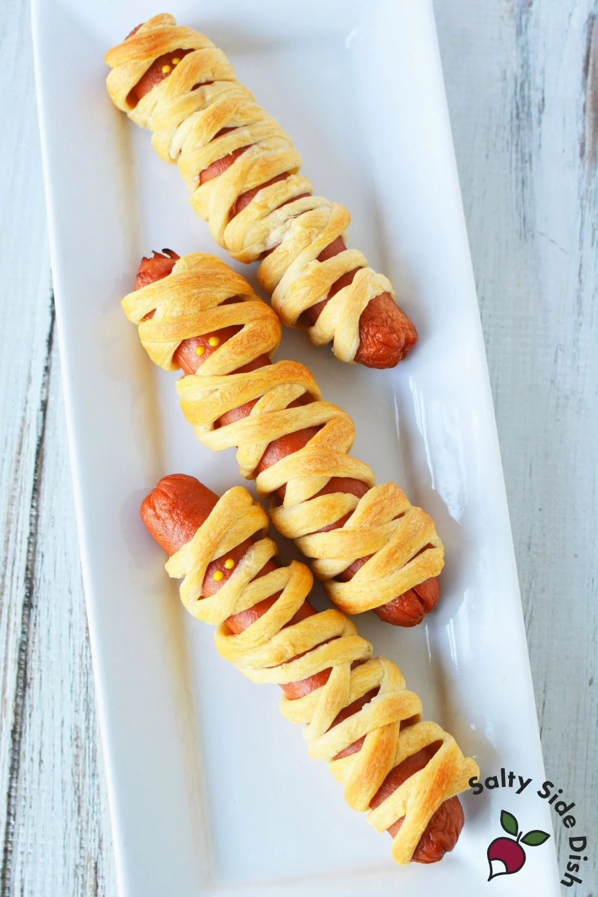 3 halloween mummy dogs on a white plate.