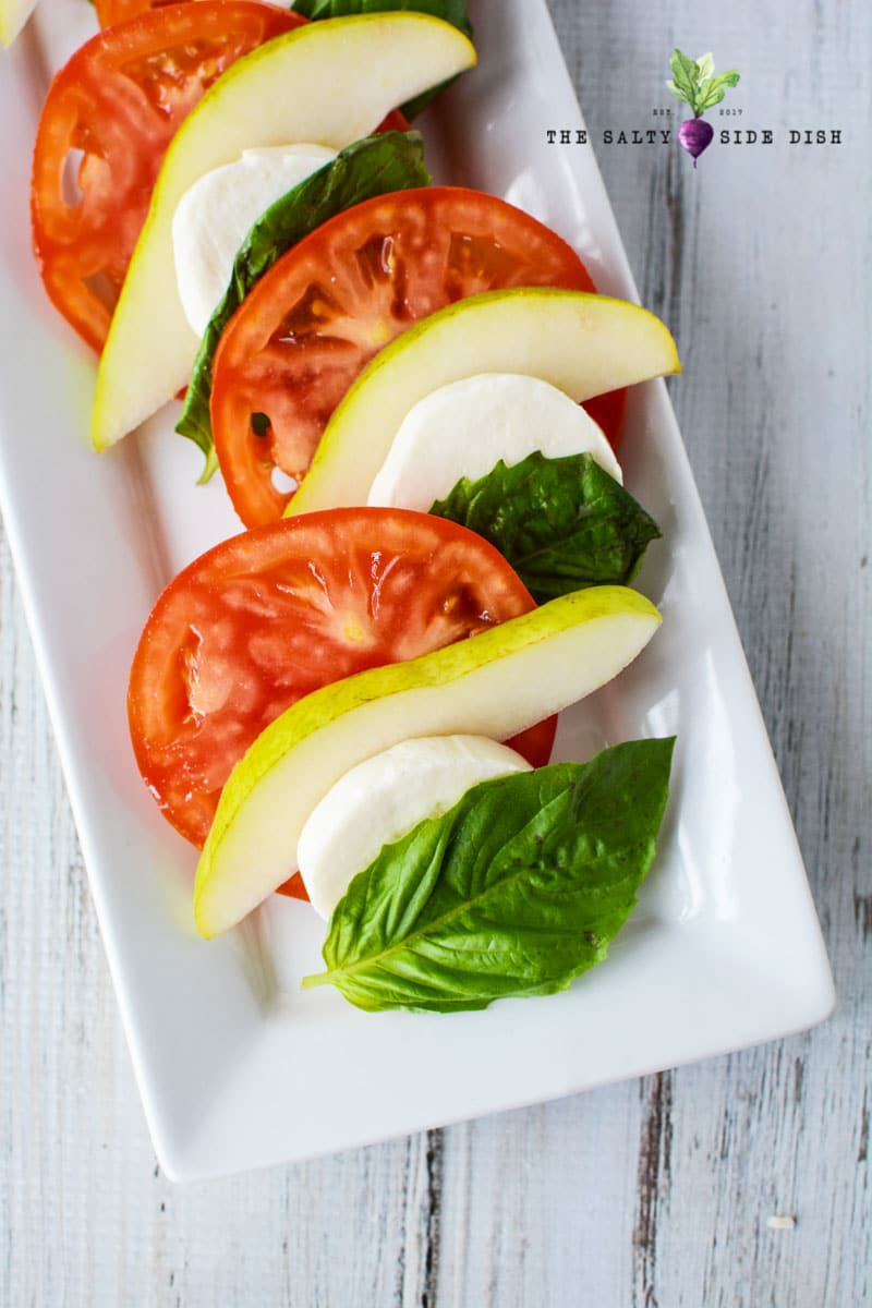 layered tomatoes, pear and basil on a white tray