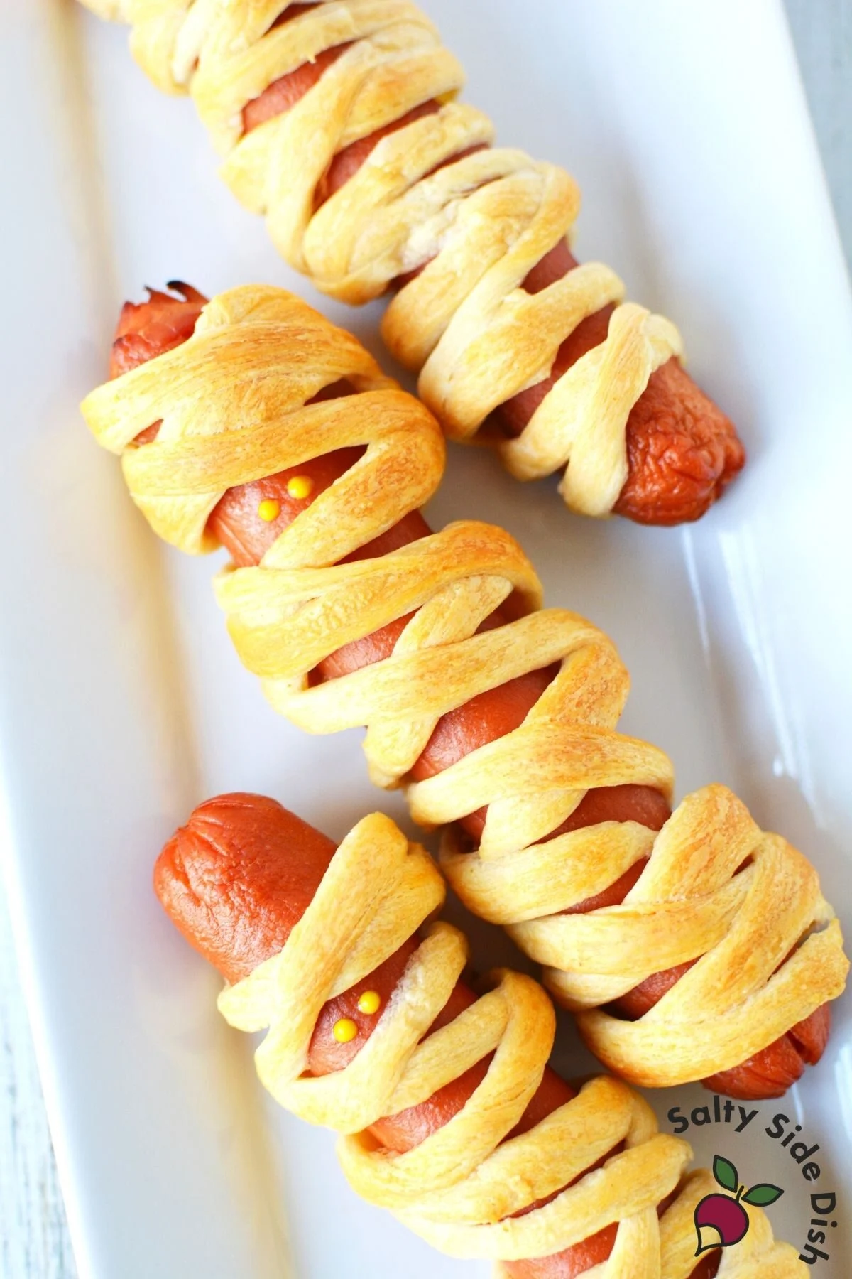 white plate with 3 mummy hot dogs.