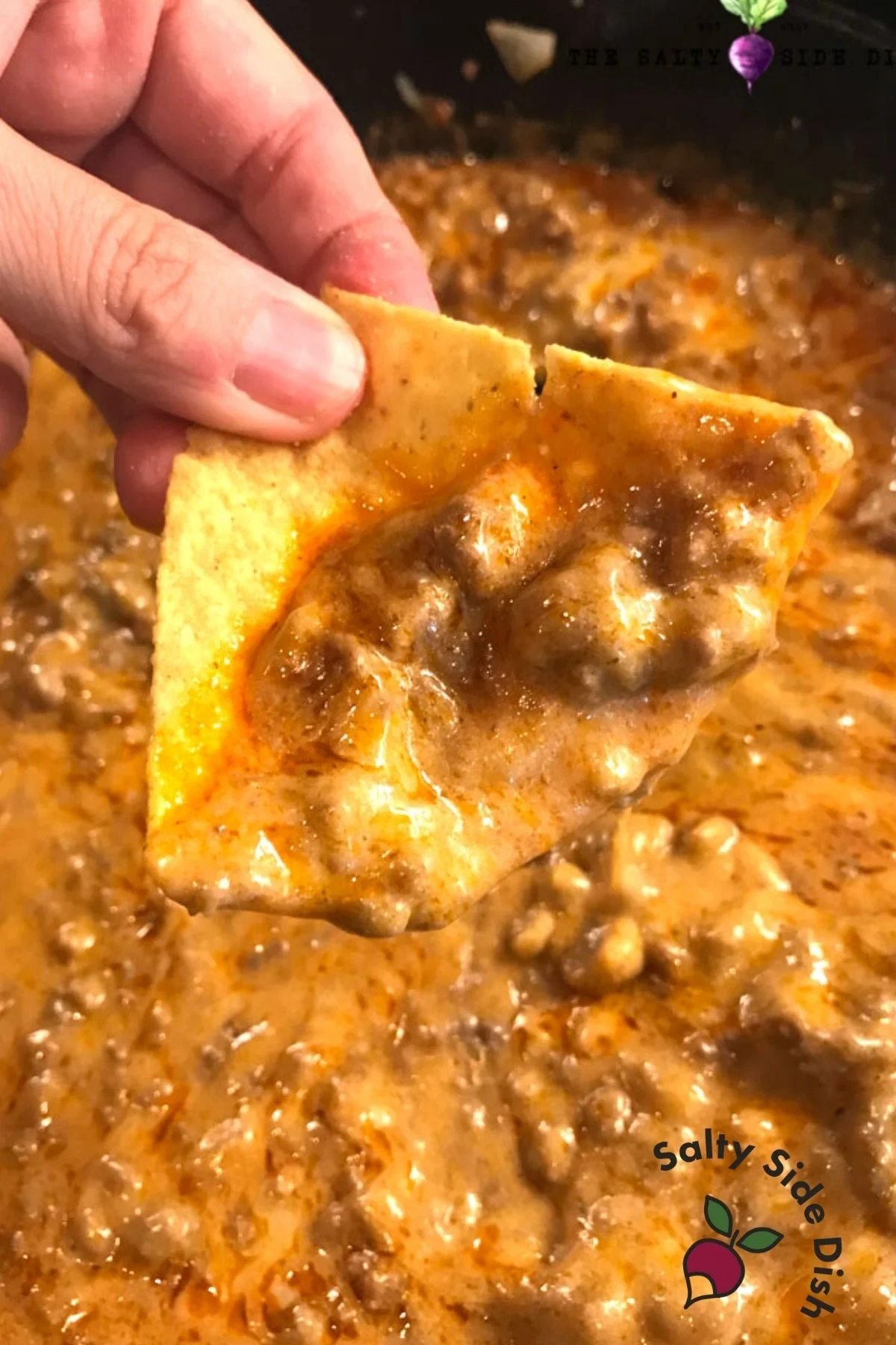 thick enchilada dip with beef on a tortilla chip being held.