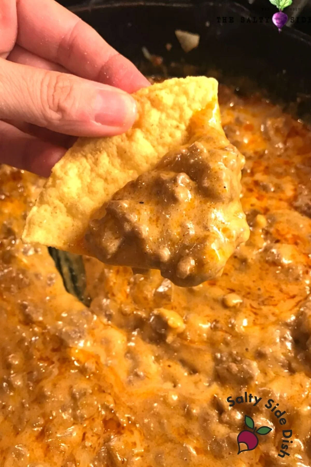 holding a beef enchilada chip with dip.