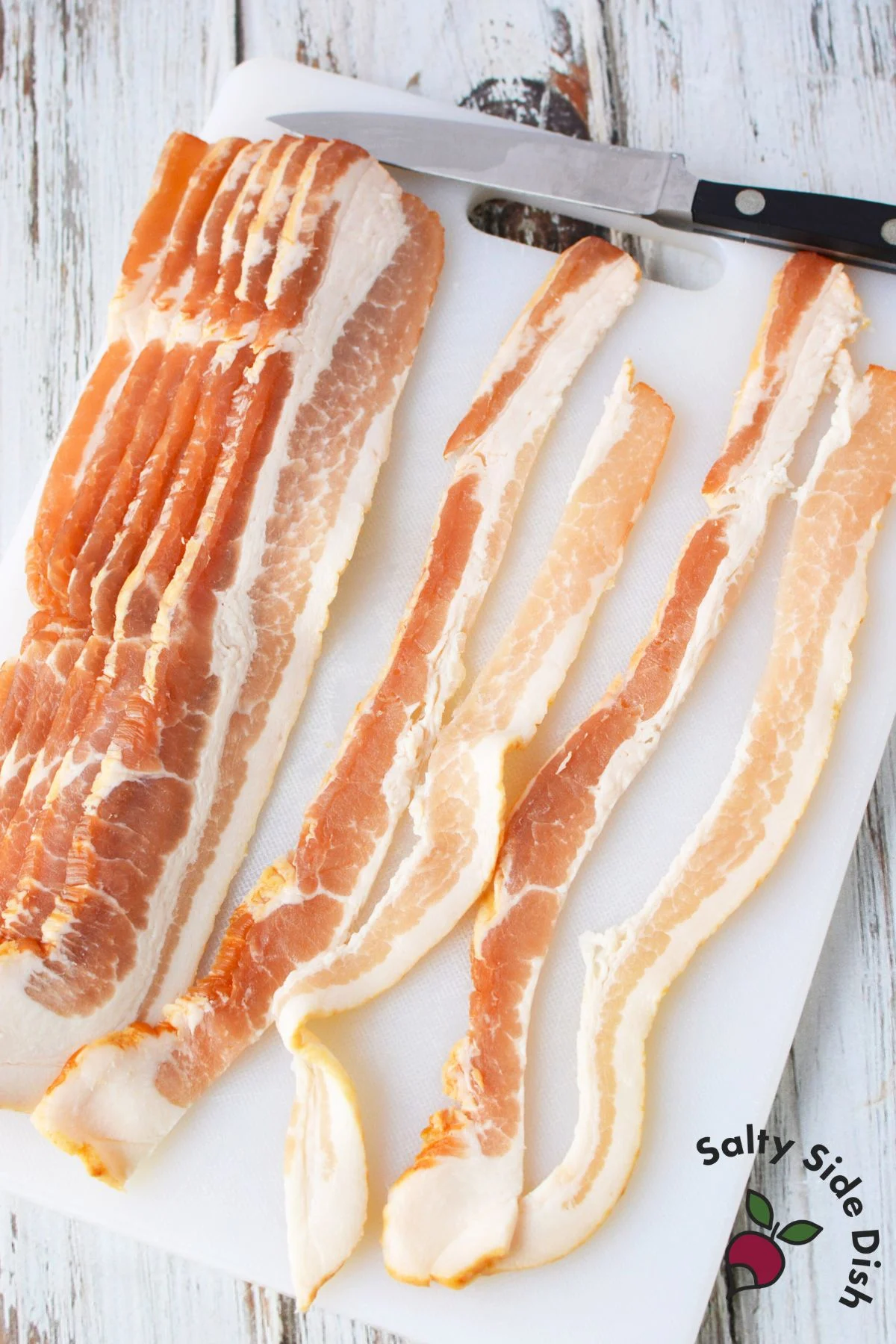 Raw bacon slices cut in half on white cutting board with knife