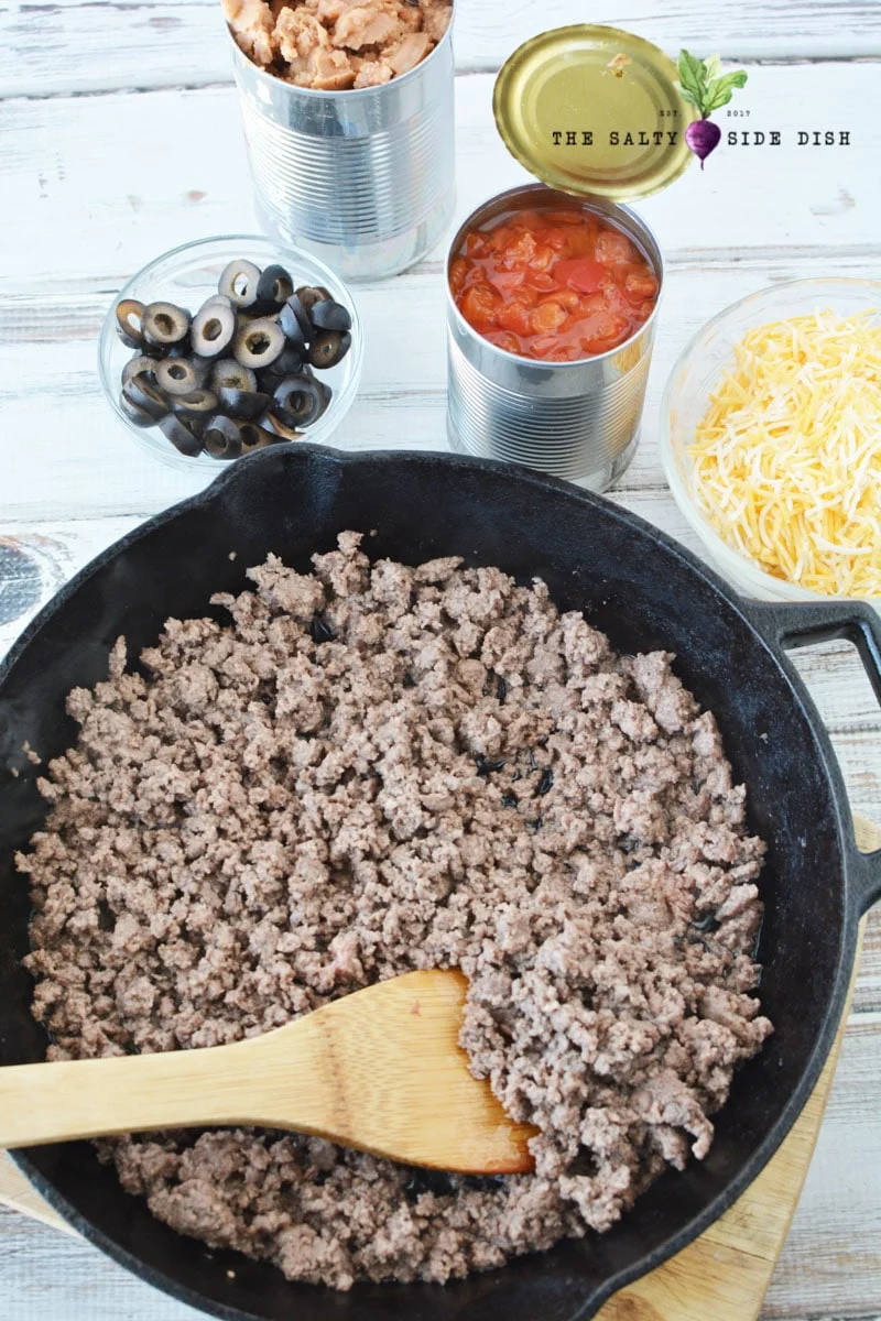 ground beef with burrito pie recipe being stirred with all measured ingredients on the side