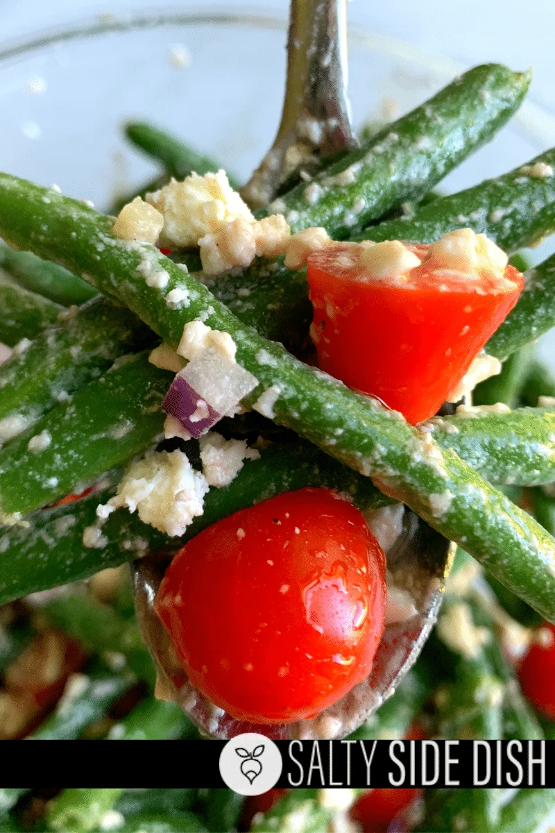 Green beans with red onion, feta, and tomatoes on a serving spoon