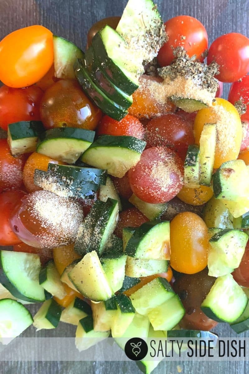 seasonings like garlic dumped over cut up cucumbers and tomatoes in a bowl