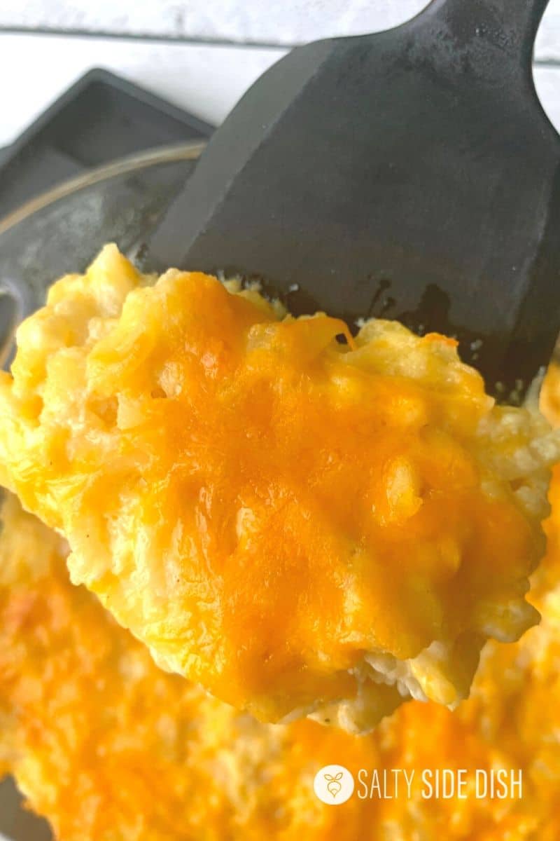 Homemade Cracker Barrel hashbrown casserole being scooped out of a baking dish with a spatula.