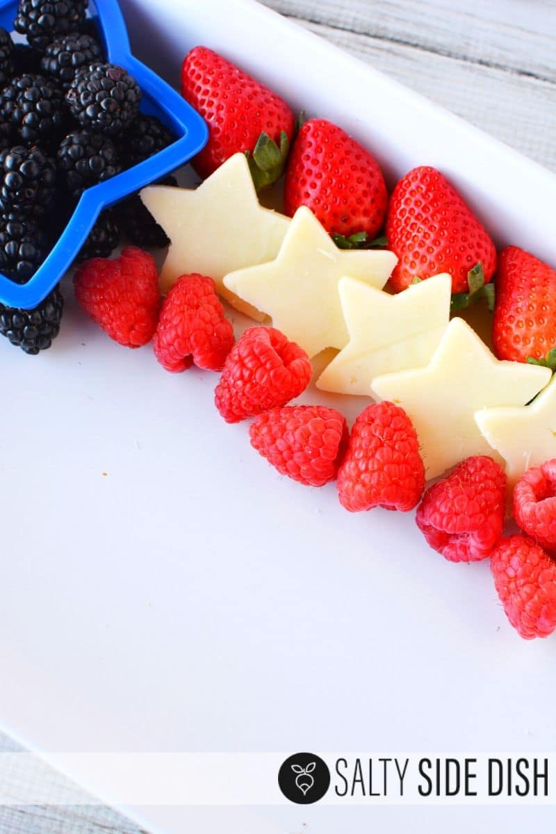 line up your red white and blue stripes for your fruit tray starting with strawberries, white cheese cut stars, raspberries, and blackberries with cookie cutters