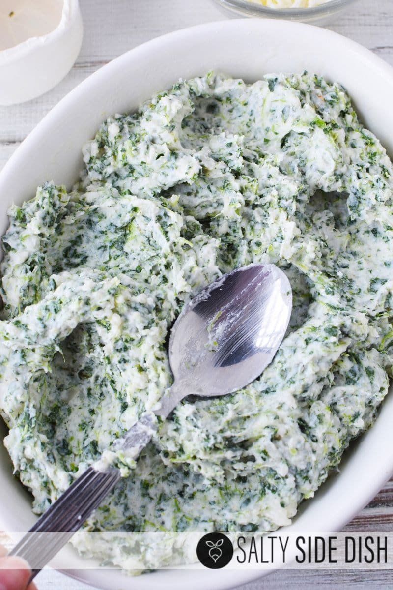Spinach Mashed Potatoes Recipe in a dish being pushed down by a spoon to even topping