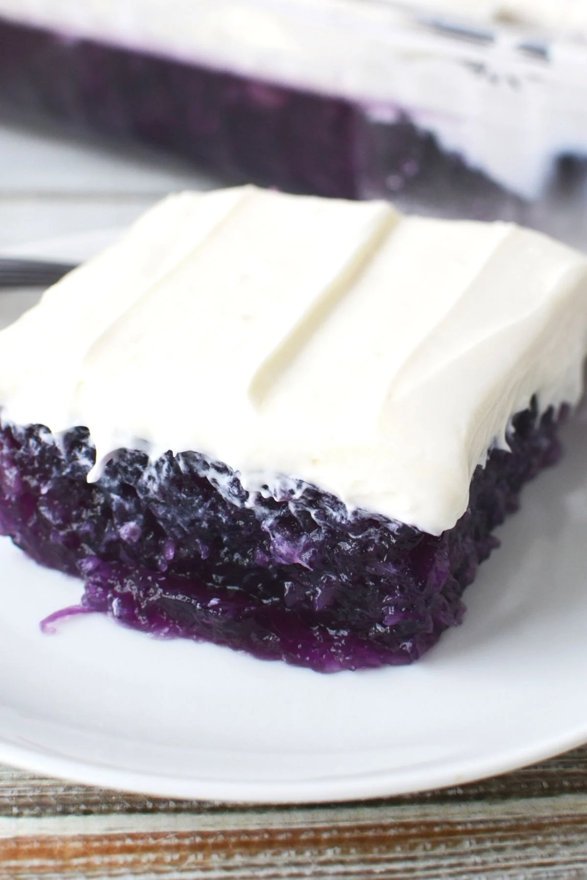 square of blueberry jello salad with cream cheese topping on a white plate.