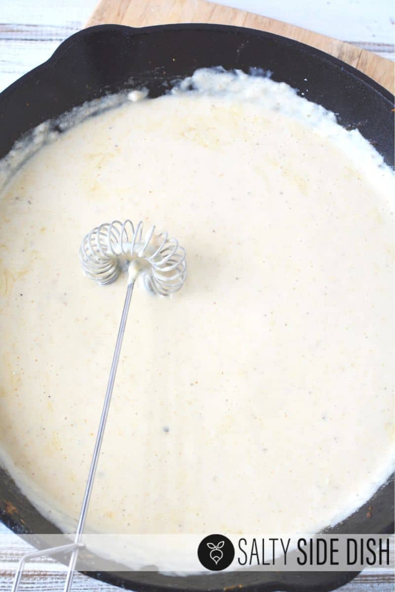 Creamy homemade base with whisk in a cast iron pan
