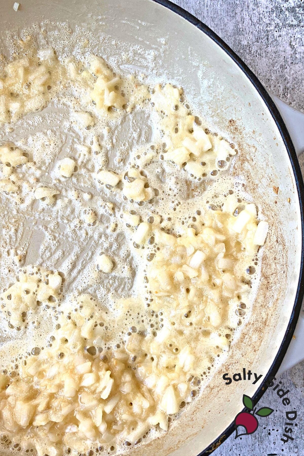 Cast Iron Mac and Cheese being made with onions, garlic, and butter in pan.