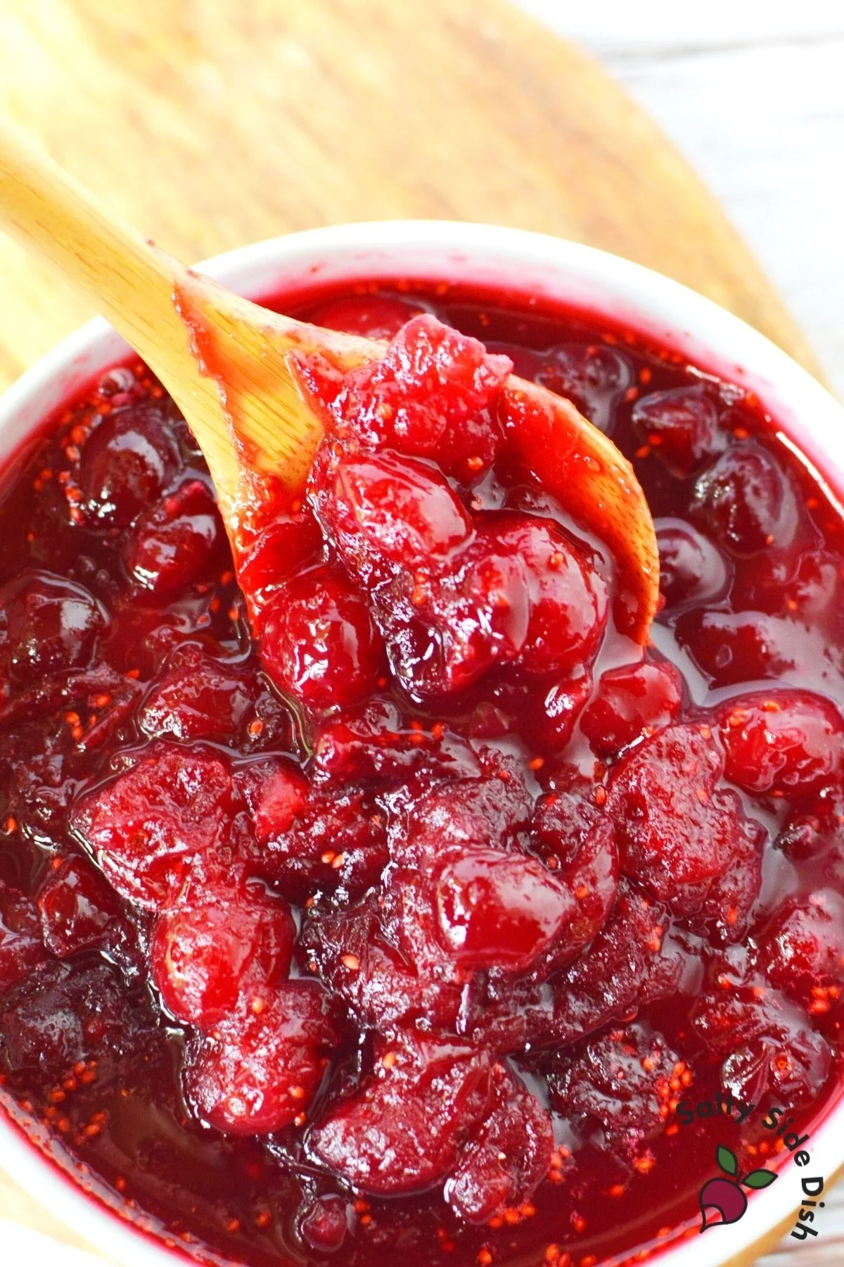 cranberry sauce in a bowl with a wooden spoon stirring sauce