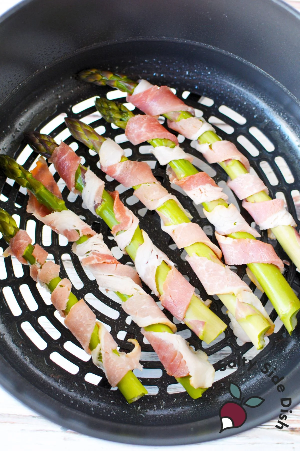bacon wrapped asparagus uncooked laying in a single layer in an air fryer basket.