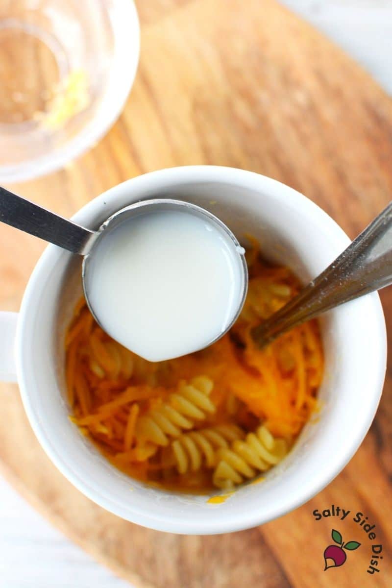 add milk and cheese into mug with cooked noodles