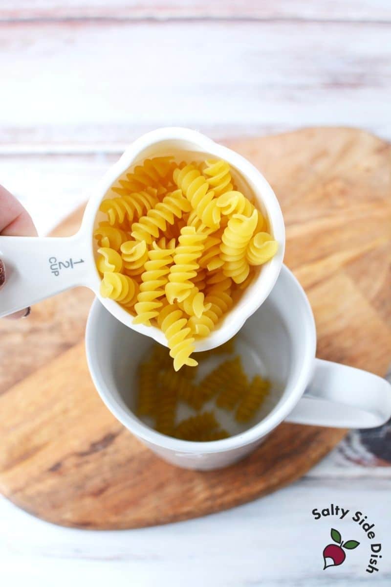 uncooked rotini noodles going into a mug
