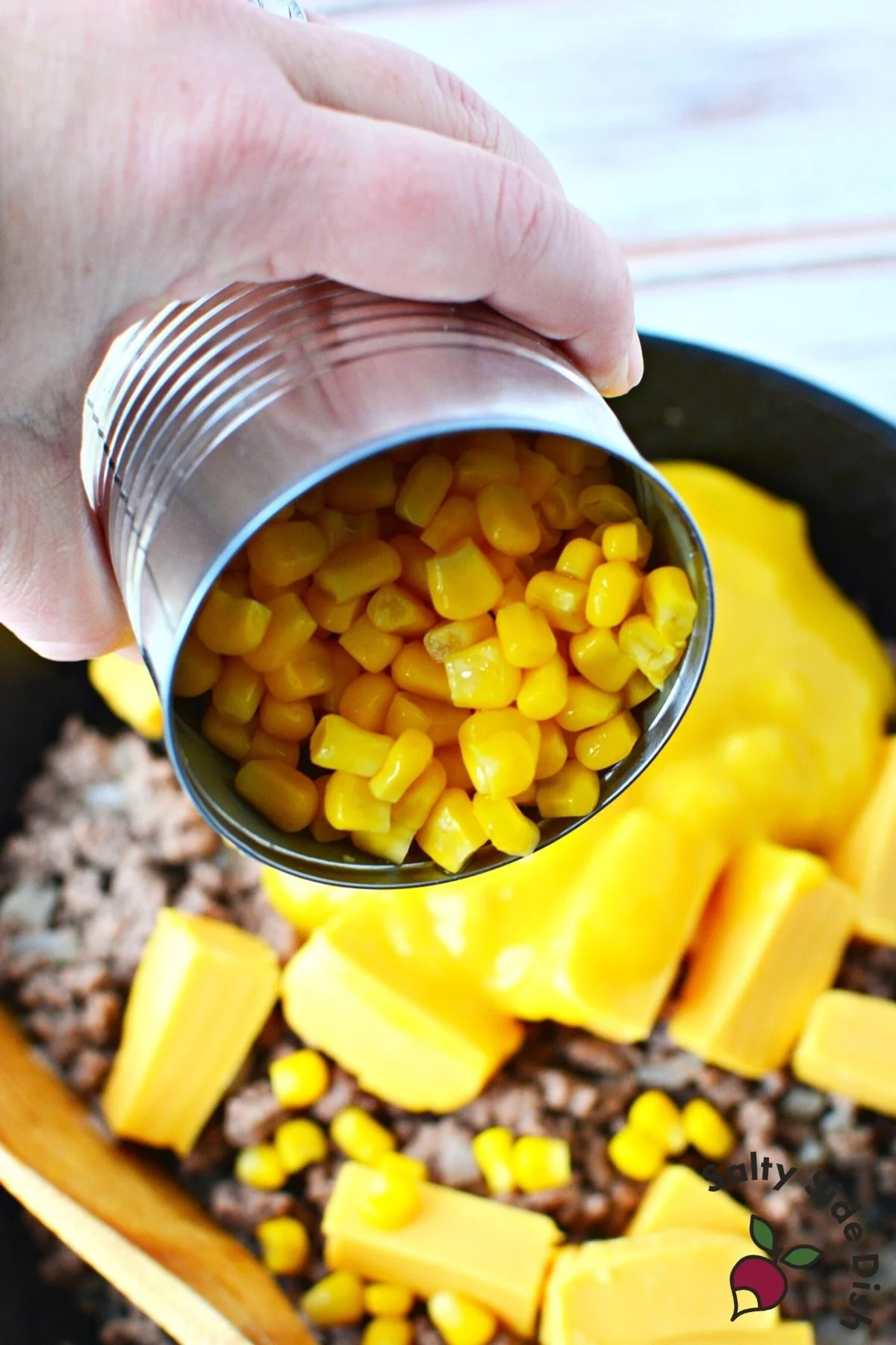 pouring corn in beef casserole recipe.