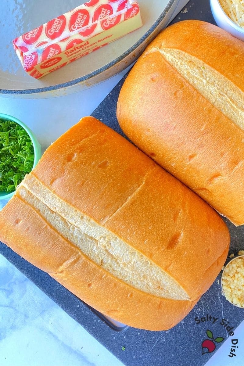 Garlic Parmesan Bread ingredients sitting on a table with butter, herbs, bread and cheese