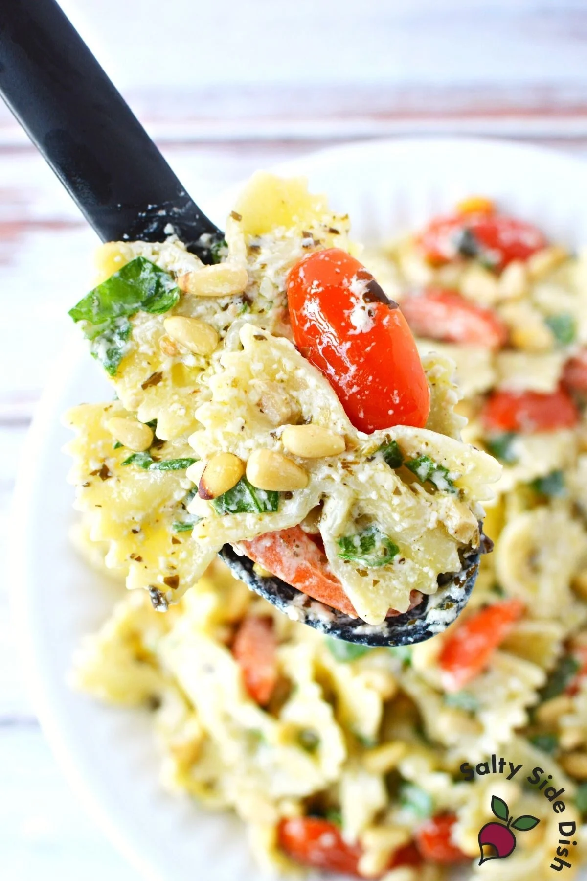 spoonfull of bowtie pasta with pesto and a tomato on top.