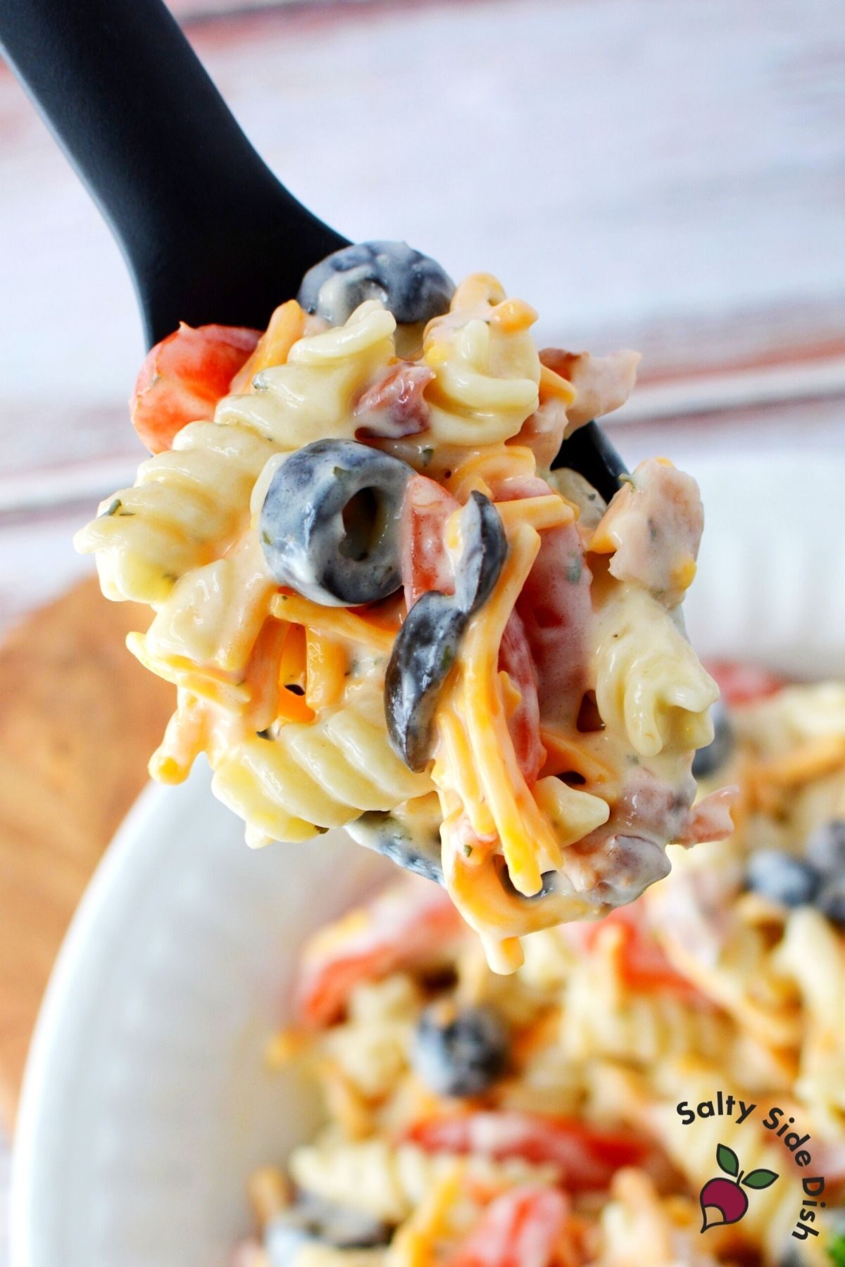 black spoon holding ranch pasta salad with olives, cheese and tomatoes visible