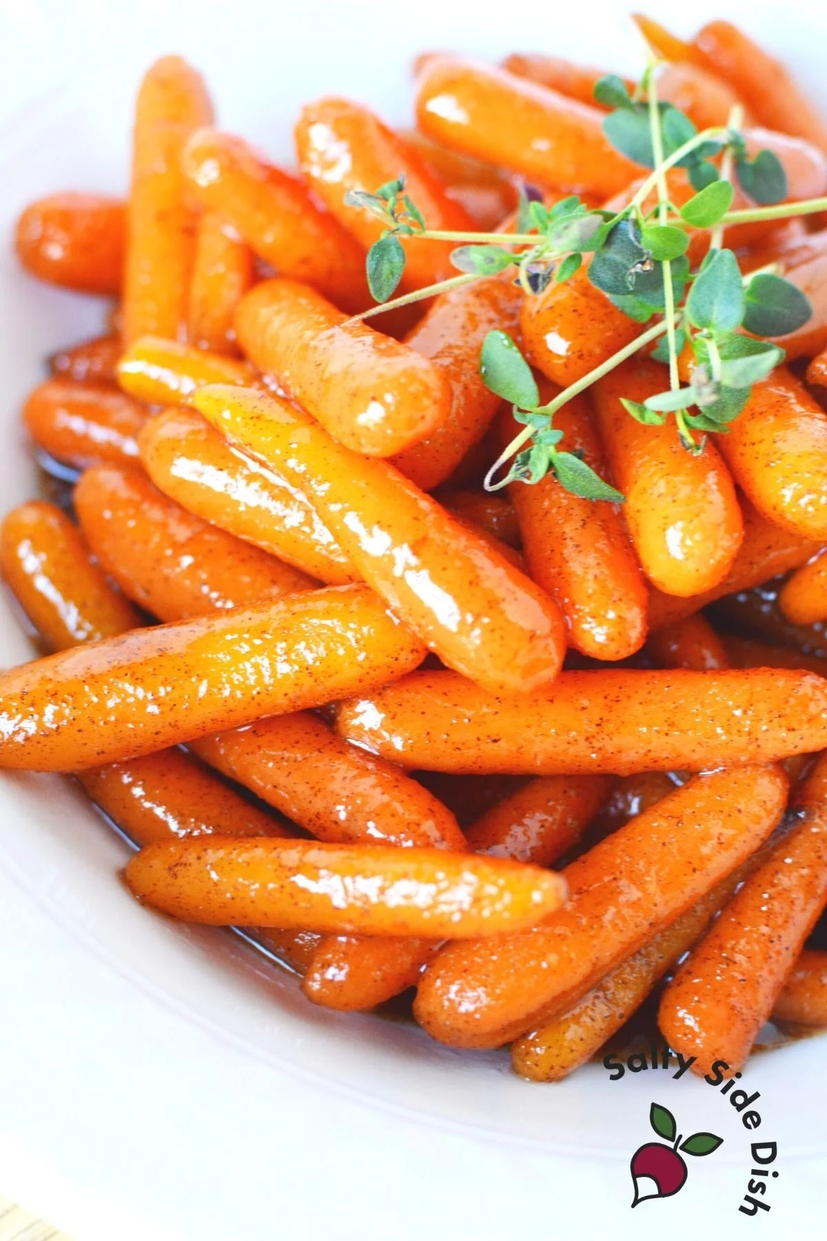 Cinnamon brown sugar glazed carrots on a white plate with herbs on top.