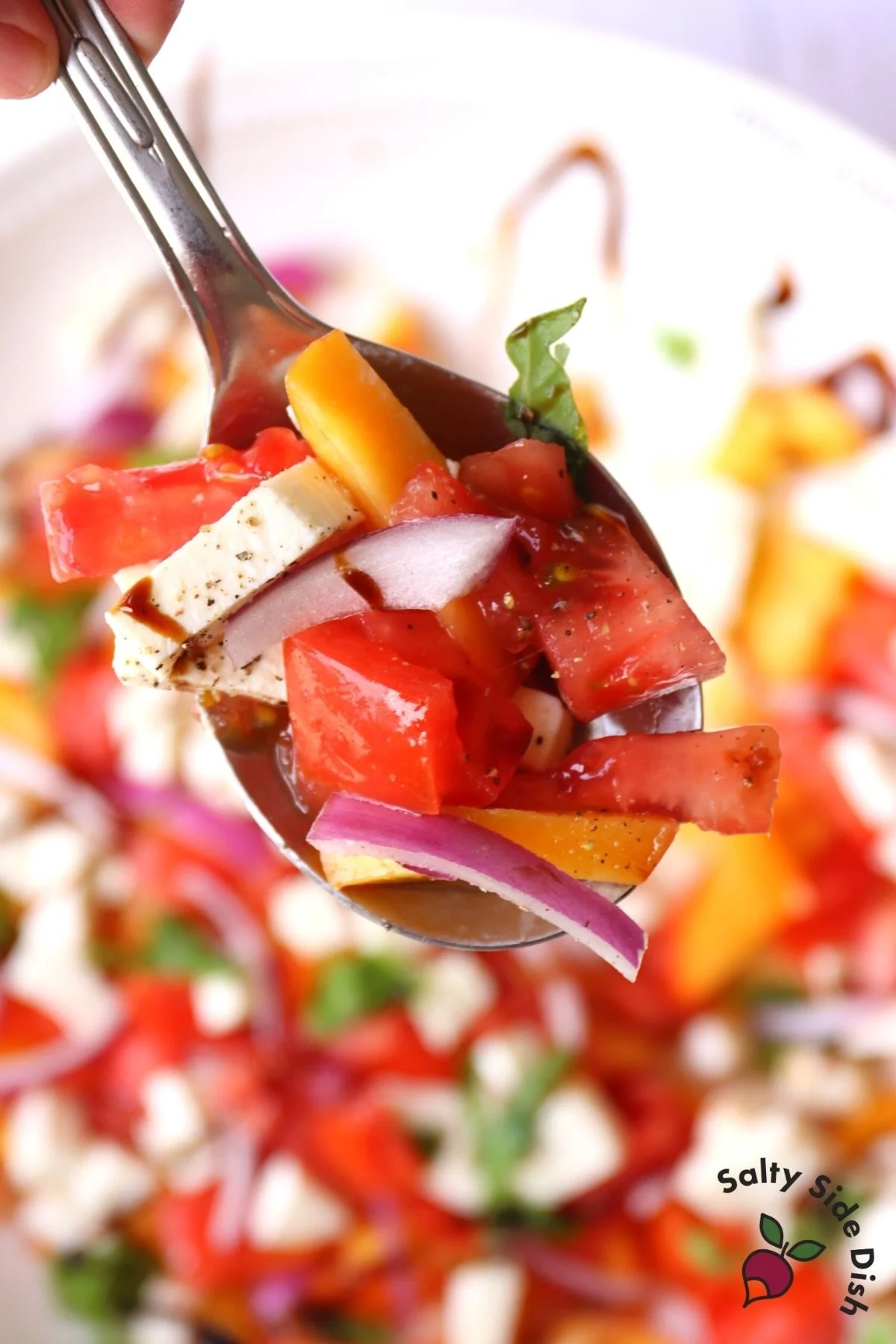 bite of caprese mozzarella salad with fresh peach slices and red onions on a spoon
