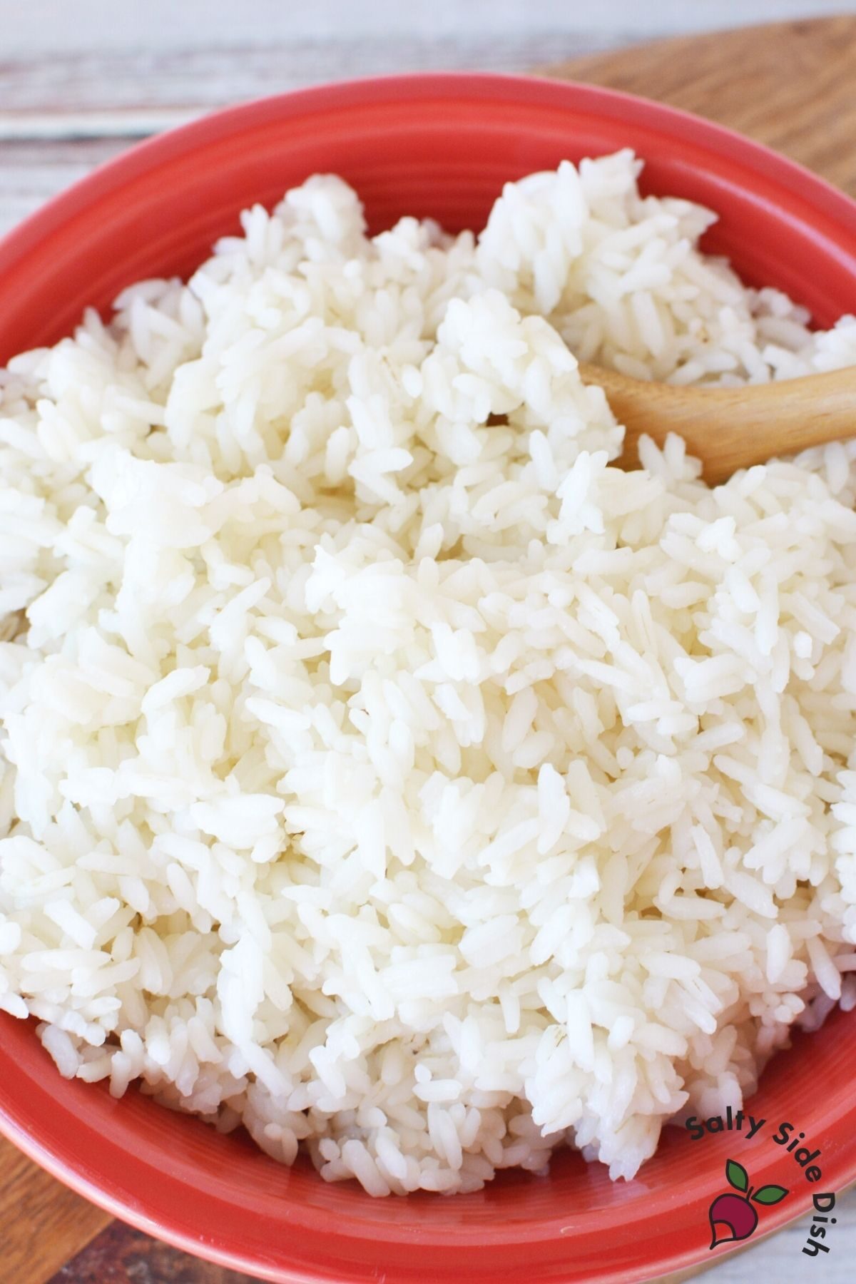 rice in a red bowl being stirred by a wooden spoon