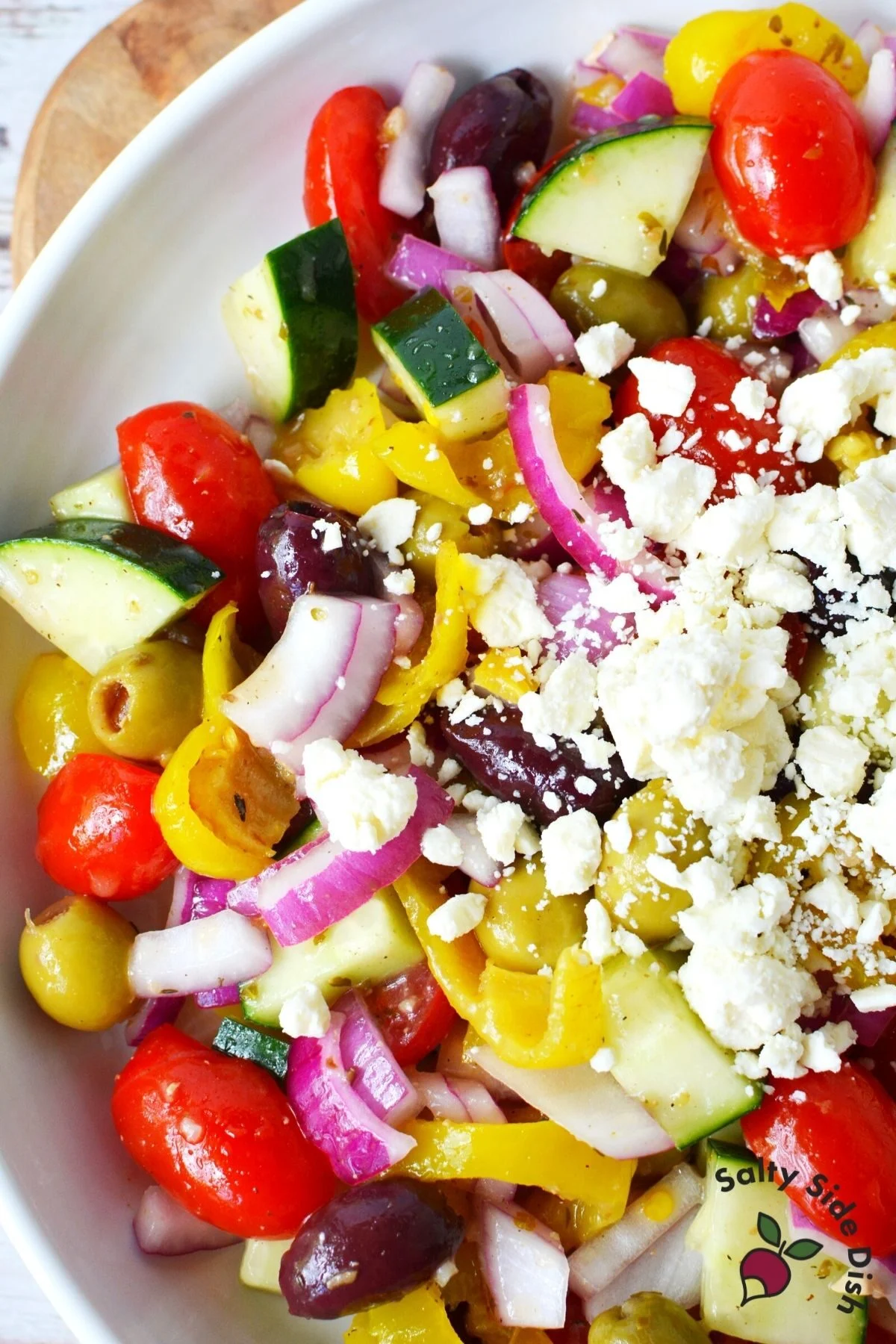 white plate with greek salad on top full of vegetables and feta cheese.
