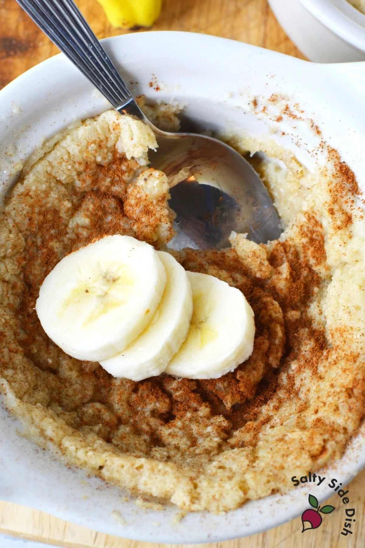 white bowl with baked oats, 3 bananas on top and a spoon inside bowl.