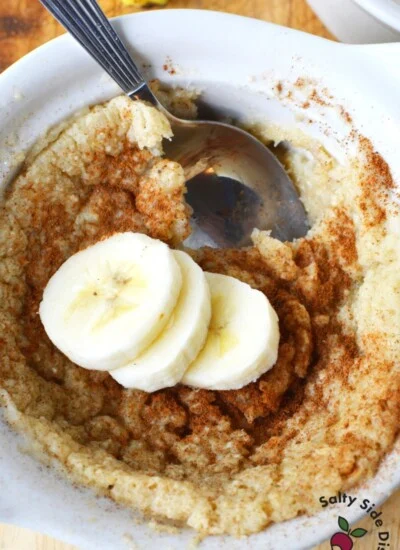 white bowl with baked oats, 3 bananas on top and a spoon inside bowl.