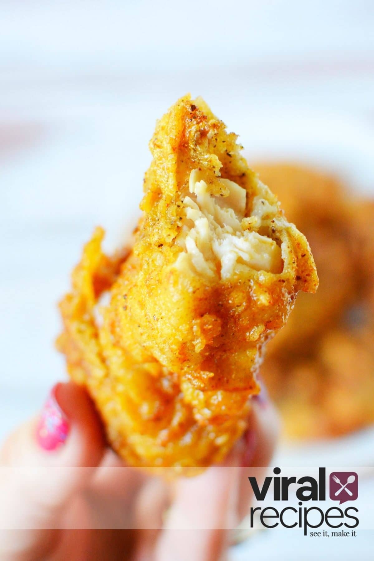 fingers holding a chicken tender with bite out of it.