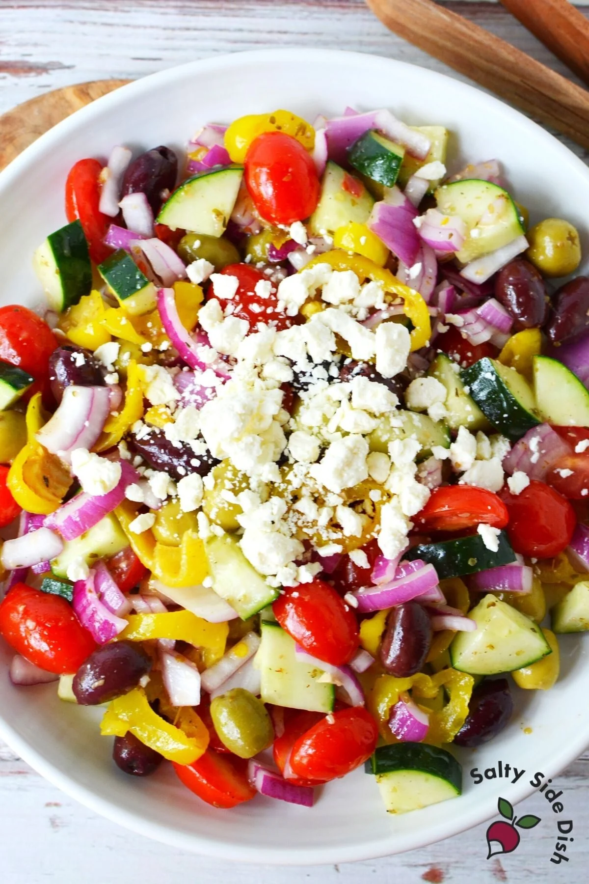 huge bowl of greek salad on a plate with feta cheese on top.
