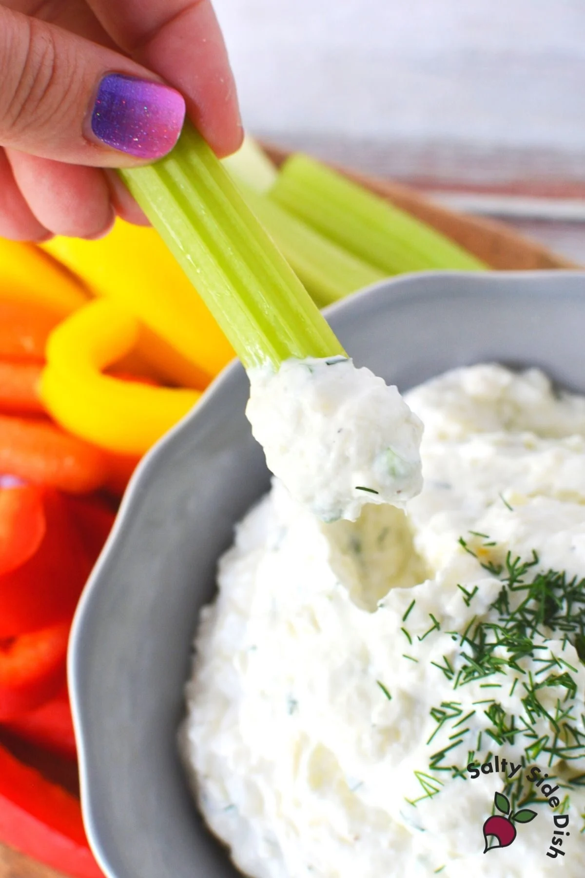 someone dipping piece of celery into garlic dip from bowl.