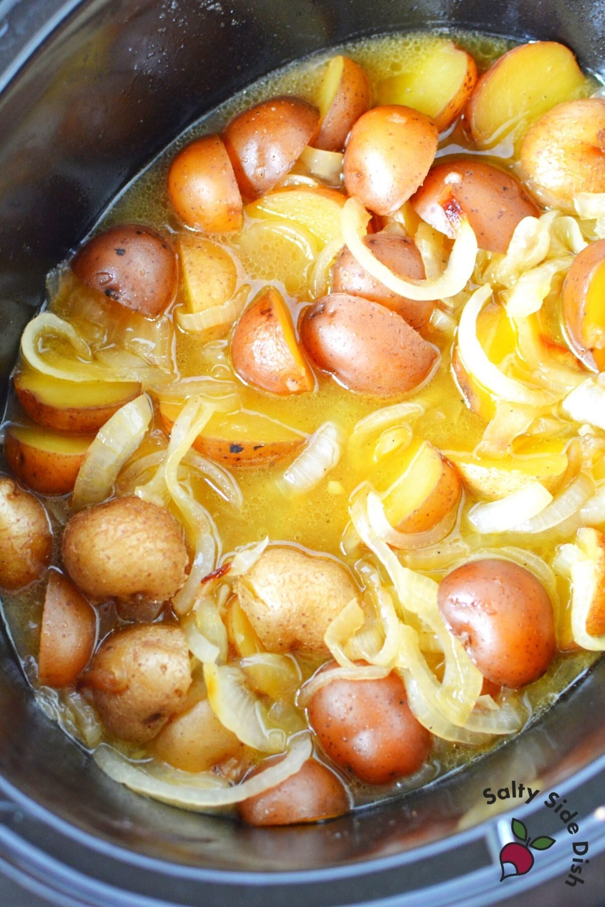 potatoes and onions in a black crockpot.