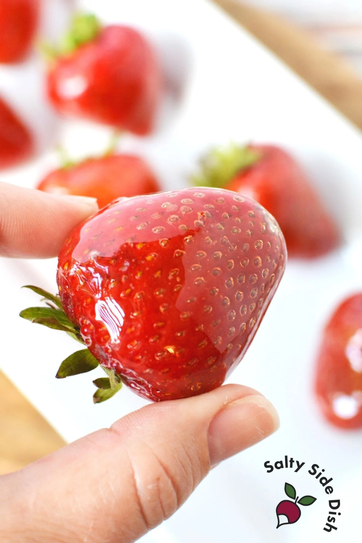 holding a tangulu candied strawberry with a finger and thumb.