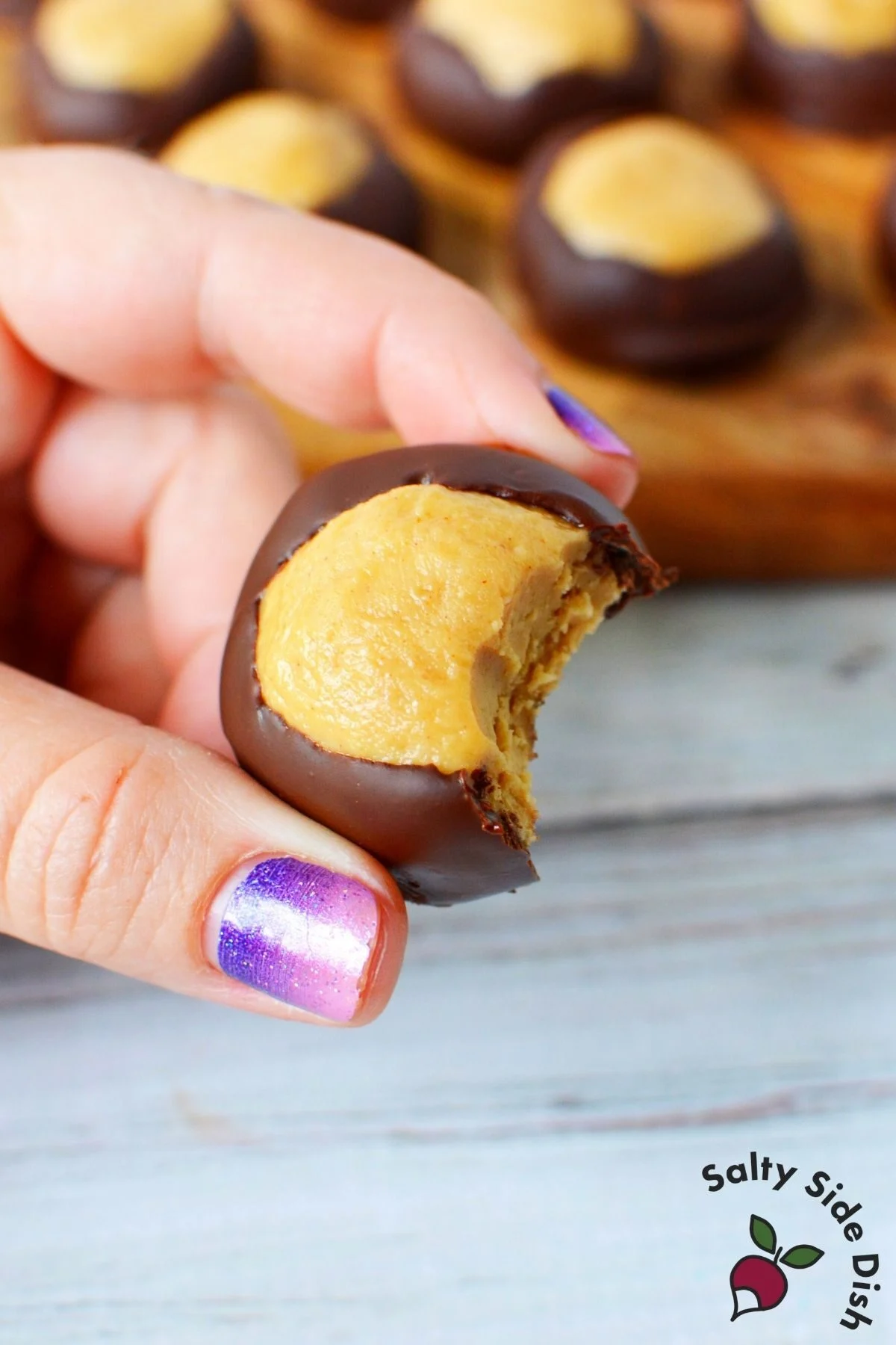 holding a chocolate covered buckeye classic treat between fingers.