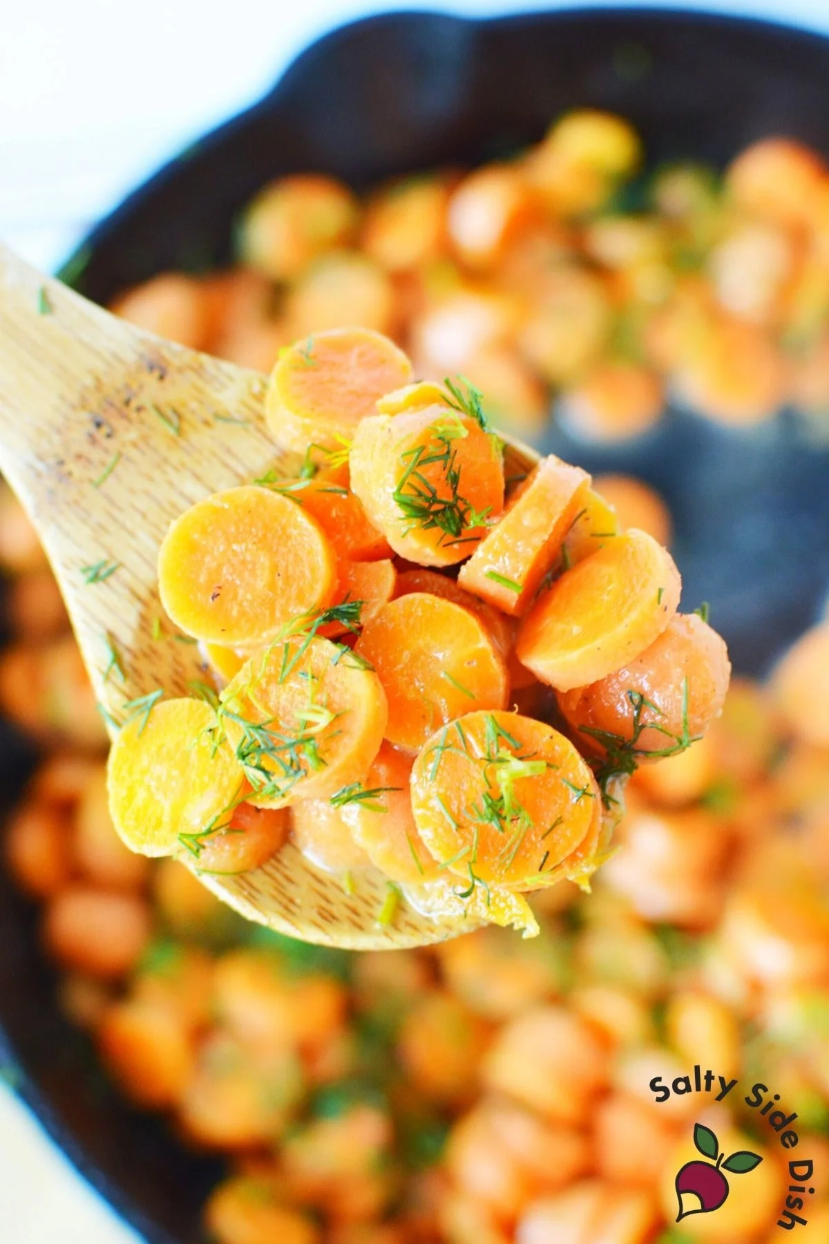 sliced carrots with dill on a wooden spoon.