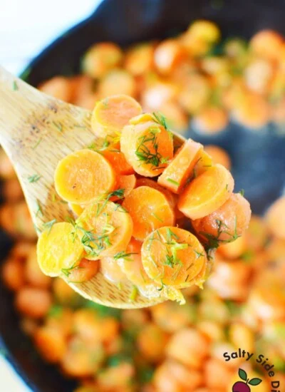 sliced carrots with dill on a wooden spoon.
