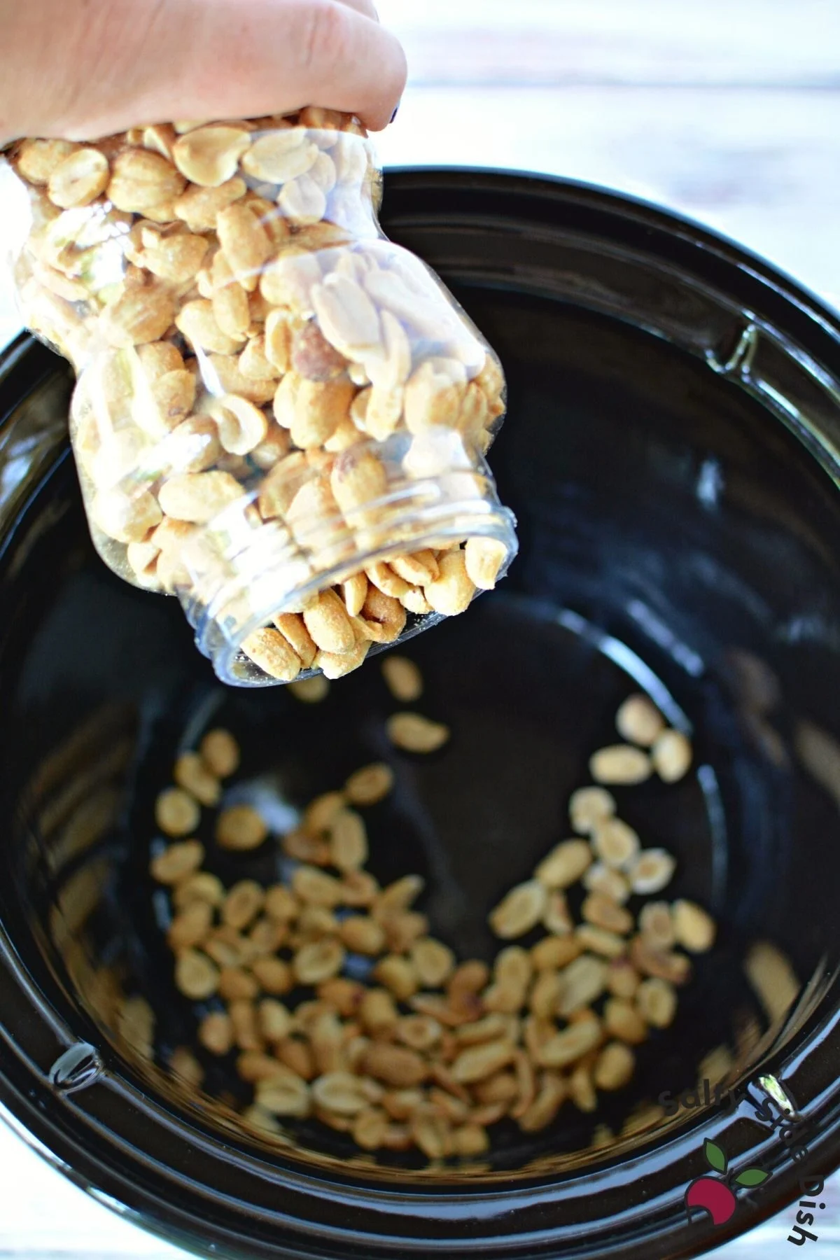 pouring a can of roasted peanuts in a crockpot.