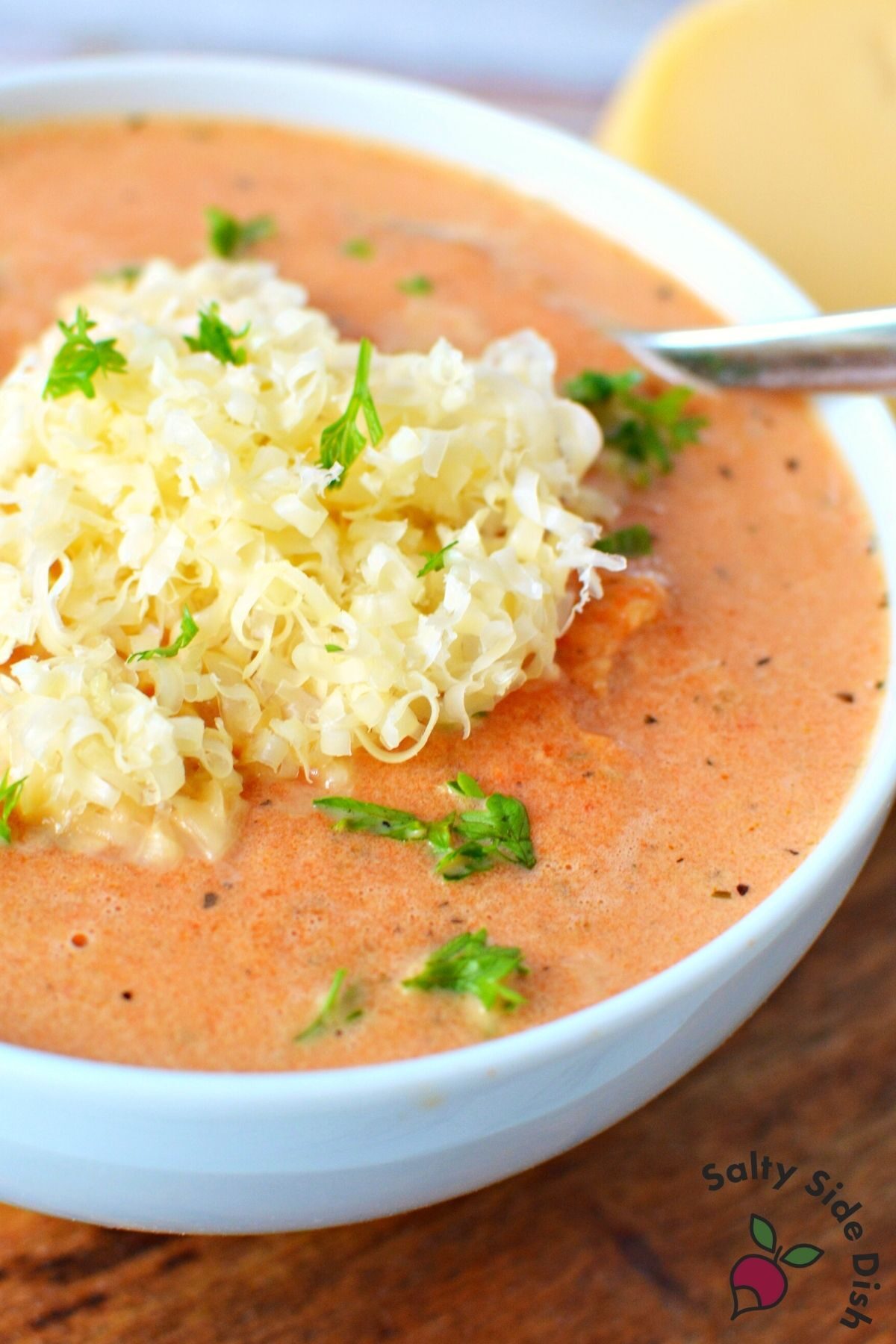 creamy red pepper soup with shredded gouda cheese on top.