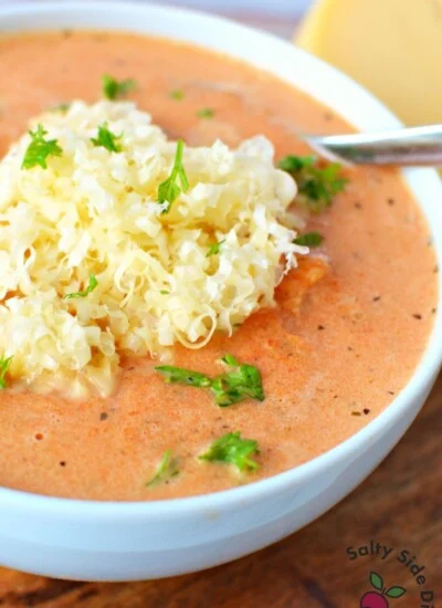 creamy red pepper soup with shredded gouda cheese on top.
