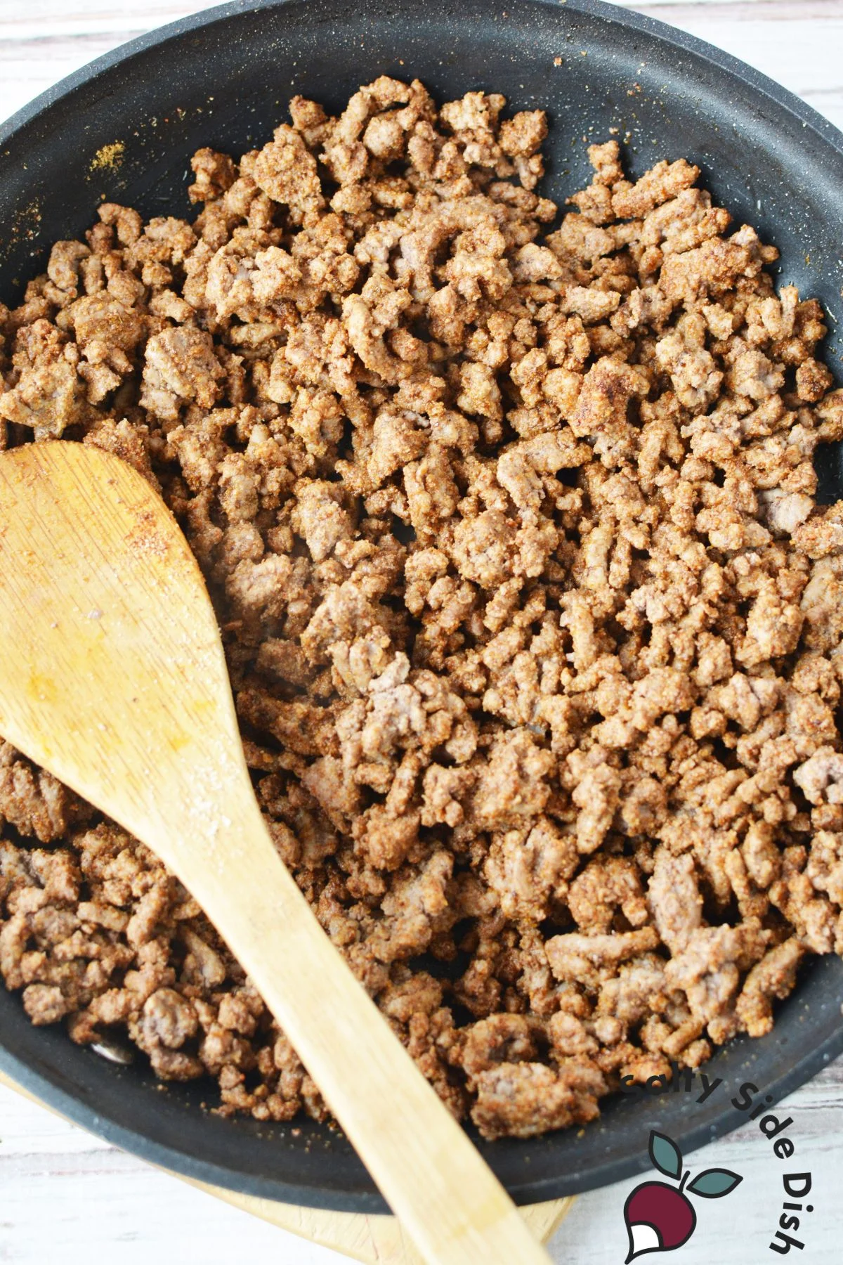 cooked ground beef in skillet being stirred by a wooden spoon.