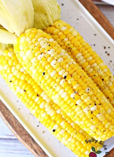 Closeup of 3 ears of boiled corn on the cob on a plate sprinkled with pepper.