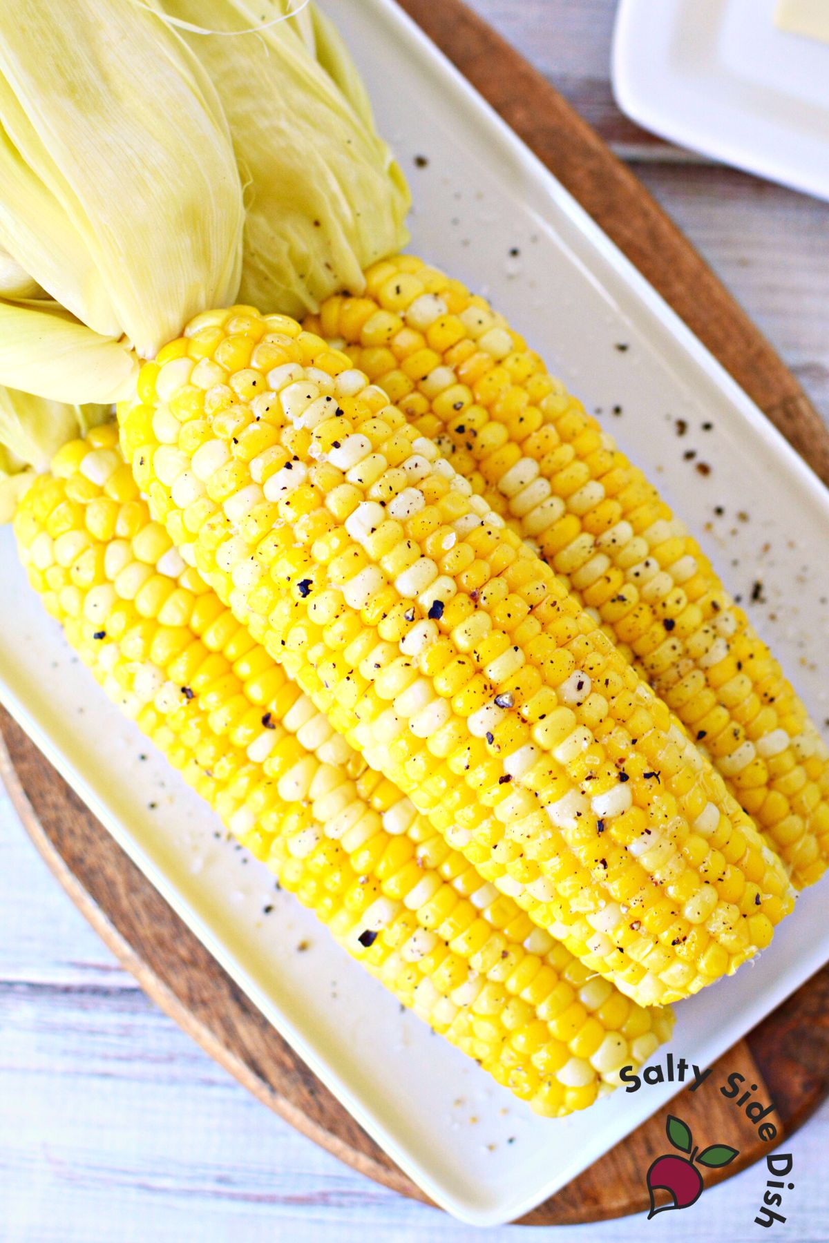 Closeup of 3 ears of boiled corn on the cob on a plate sprinkled with pepper.